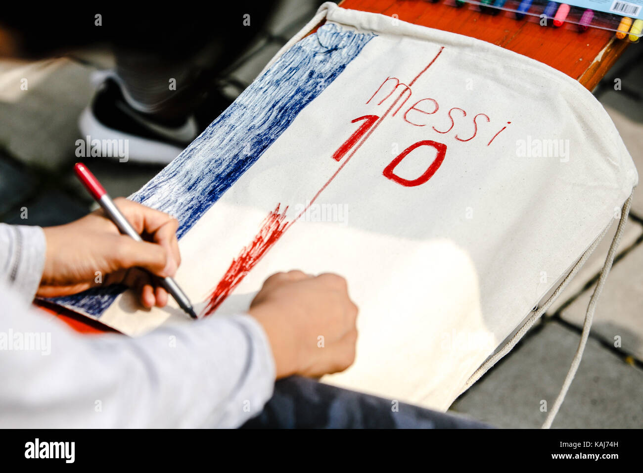 Ein Kind malt das Jersey der Fußballer Lionel Messi auf eine Sporttasche mit einem Marker Stockfoto