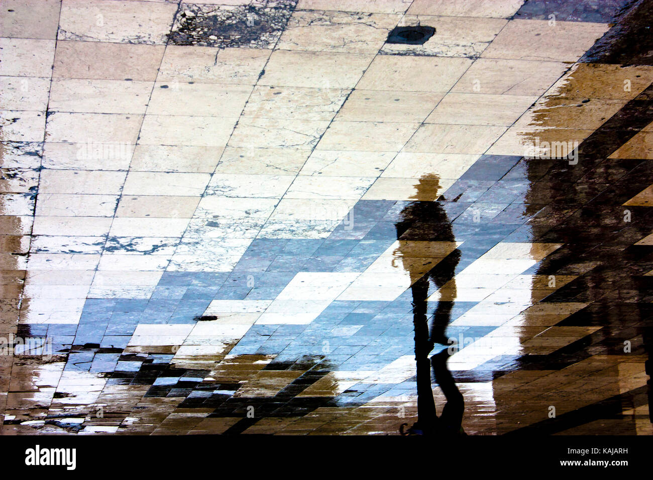 Unscharfe Reflexion Schatten Silhouette eines einzelnen Mannes zu Fuß in die Altstadt Fußgängerzone kurz nach dem Regen, mit Hut und gefalteter Regenschirm Stockfoto