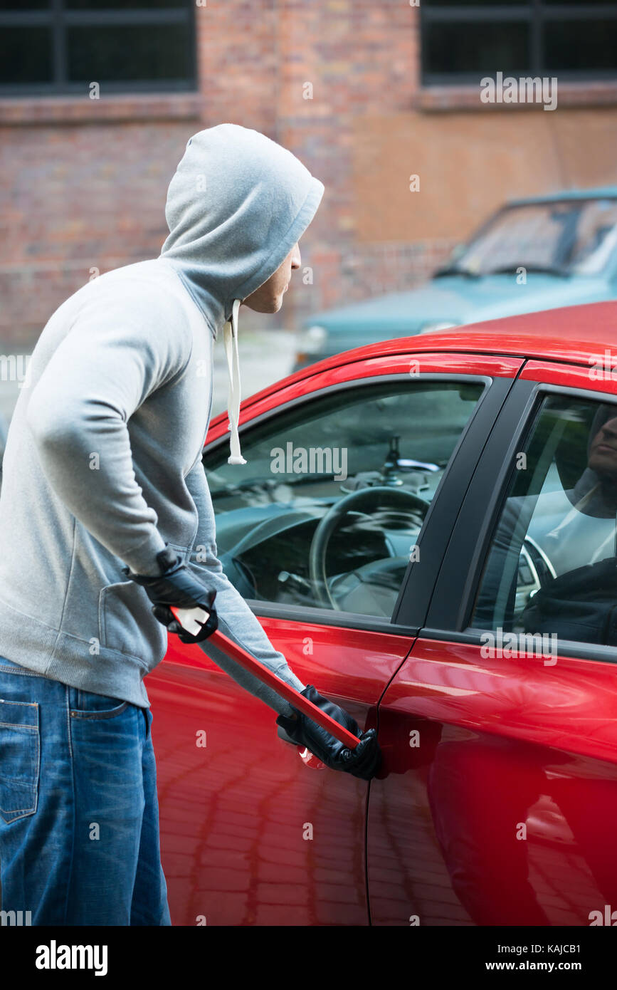 Dieb in Kapuzenjacke mit Brecheisen an offene Autotür Stockfoto