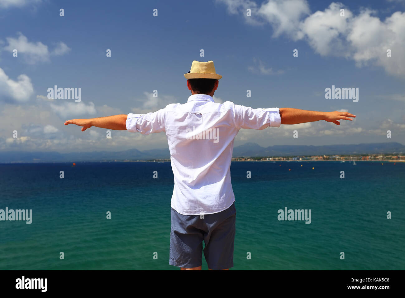 Mann mit Hände weit auf dem smaragdgrünen Mittelmeer Hintergrund geöffnet. Junge im Sommer Hut und weissen Hemd an italienischen Resort. Stockfoto