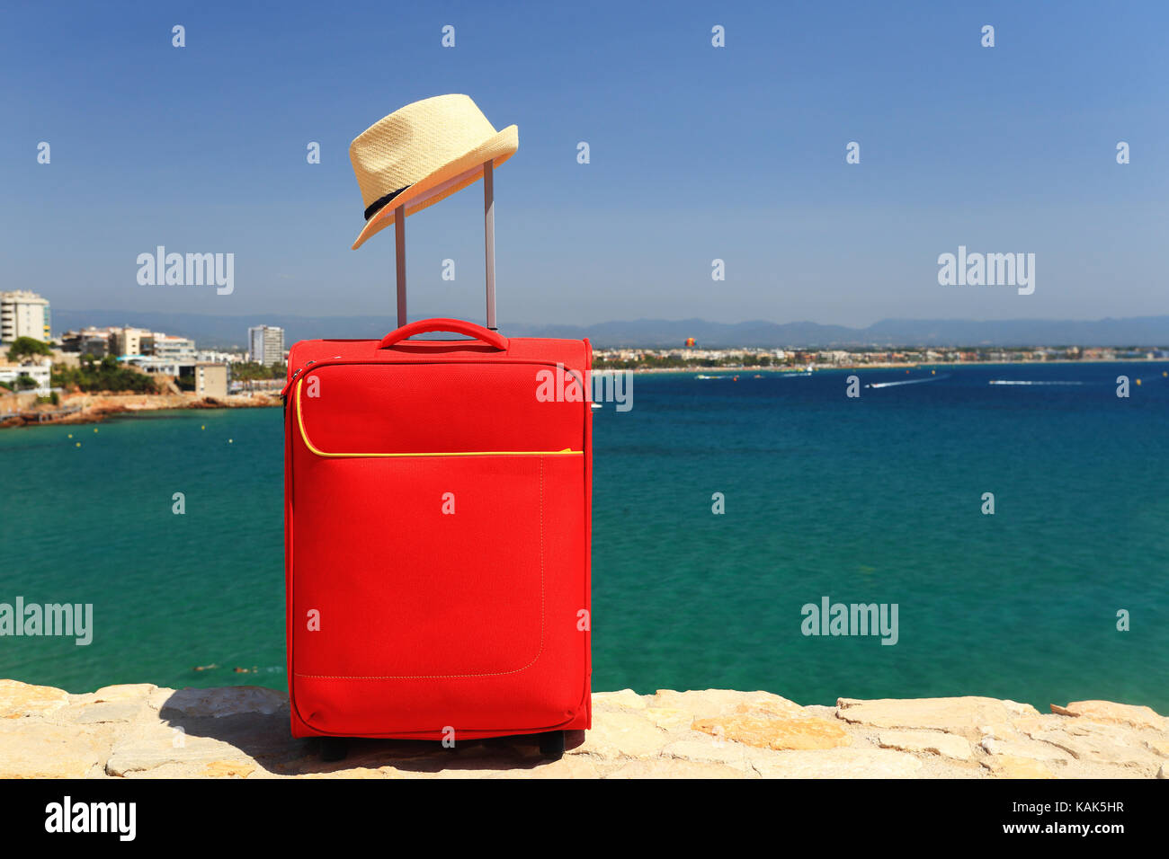 Resort und Travel Concept. Ferienhäuser Hintergrund. Roten Koffer und Sommer Hut auf dem Meer im Hintergrund. Sonnigen Sommertag in Salou, Spanien Resort. Stockfoto
