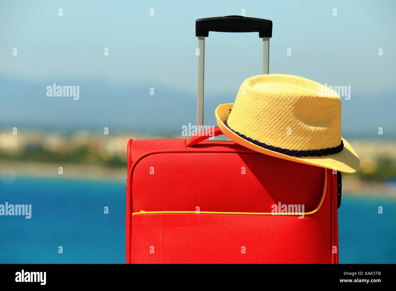 Sommer Hut auf dem roten Koffer close-up. Urlaub und Reisen Konzept. Koffer und gelben Hut auf sonnigen Meer Hintergrund. Stockfoto