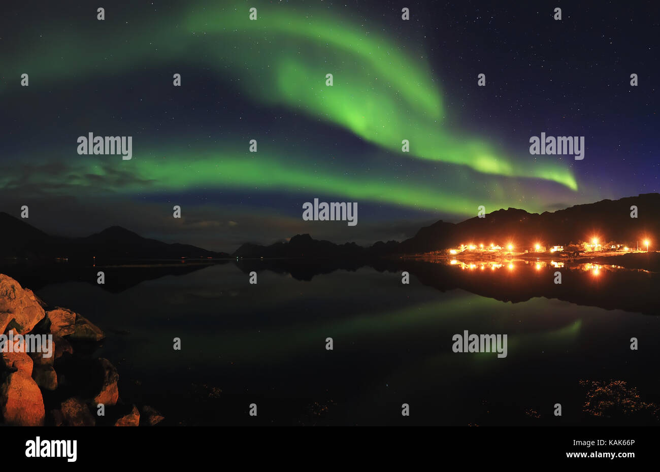 Grüne Polarlichter in der Nacht Sternenhimmel. Northern Lights reflektieren in See in kleinen norwegischen Stadt. Schönen Norden Nacht Landschaft. Stockfoto