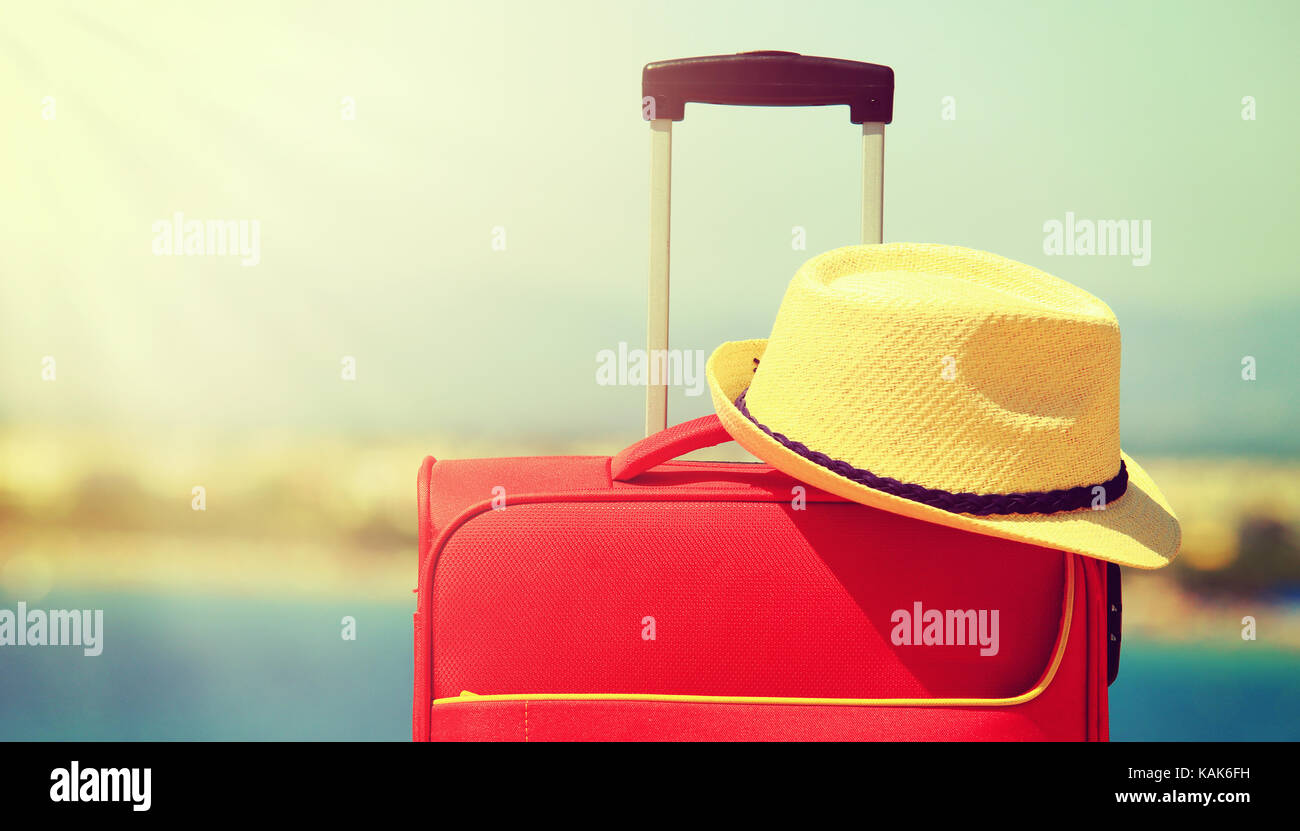 Hat und Red Koffer Nahaufnahme. Sommer Urlaub und Reisen Konzept. Koffer und gelben Hut auf weichen Meer Hintergrund. Stockfoto