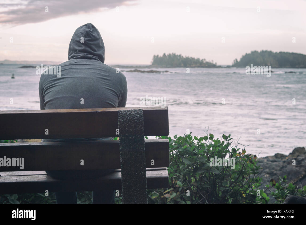 Traurig und einsam Mann sitzt auf der Bank mit Blick auf das Meer auf Vancouver Island Stockfoto