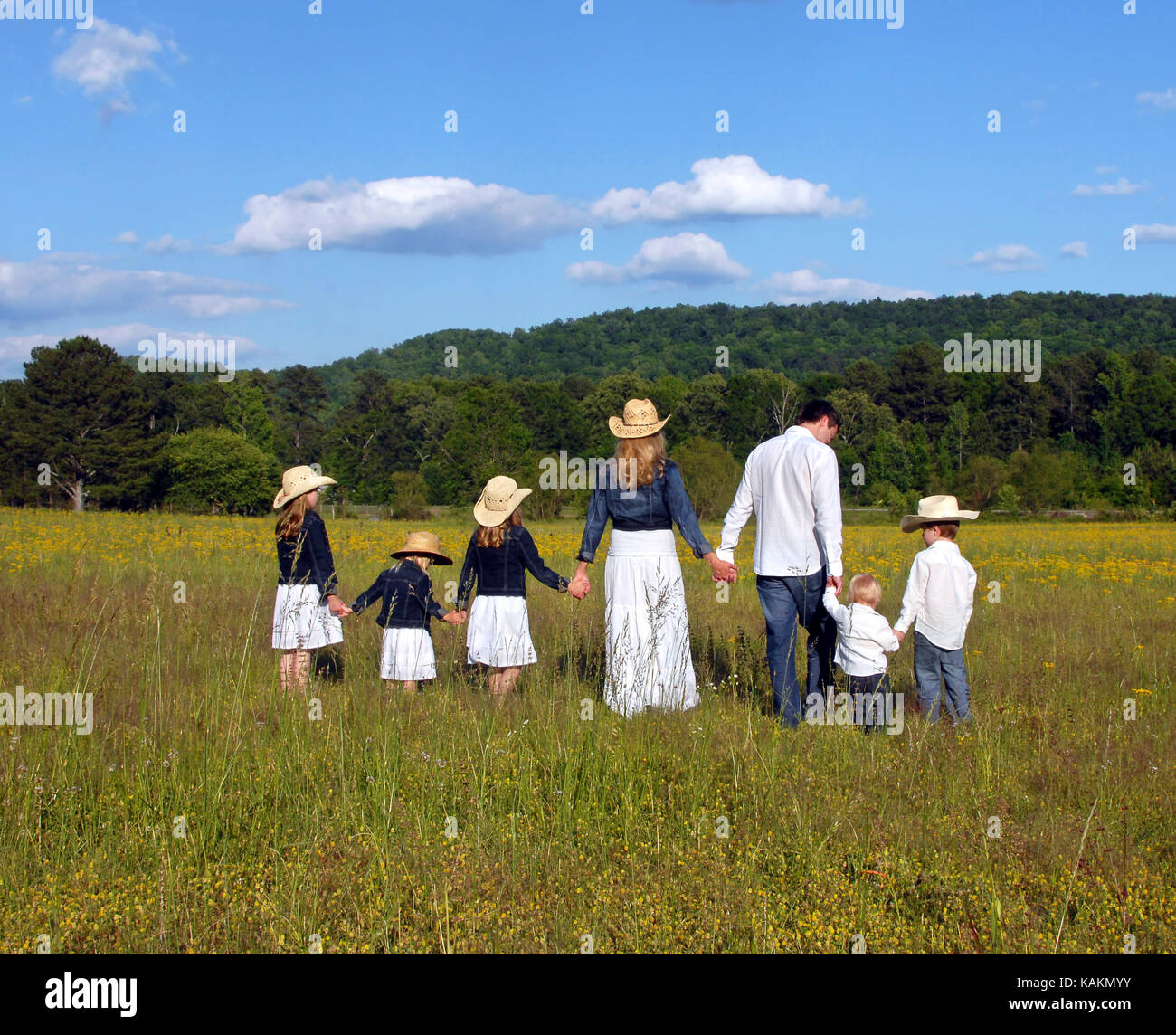 Mama und Papa führen Kinder über offenes Feld von gelben Blumen in ländlichen Alabama. Alle halten sich an den Händen. Stockfoto