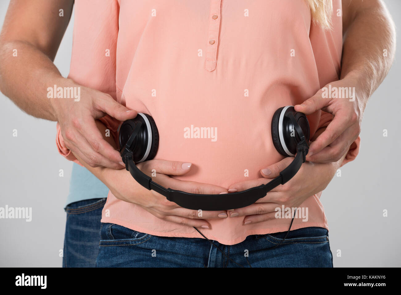 Mittelteil der Mann mit Kopfhörer auf den schwangeren Bauch auf weißem Hintergrund Stockfoto
