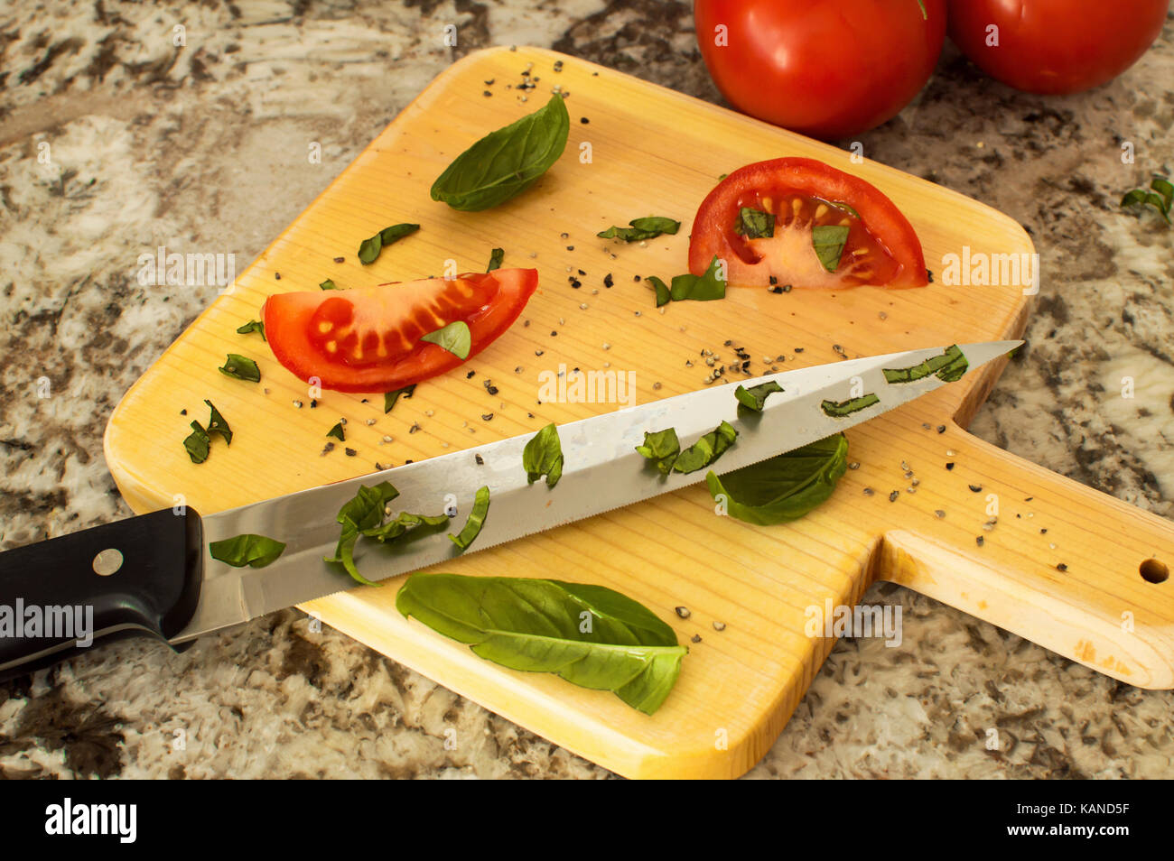 Eine in Scheiben geschnittene Tomaten mit Basilikum auf einem Schneidebrett mit einem kochmesser und ein Bündel von Tomaten auf der Rebe. Stockfoto