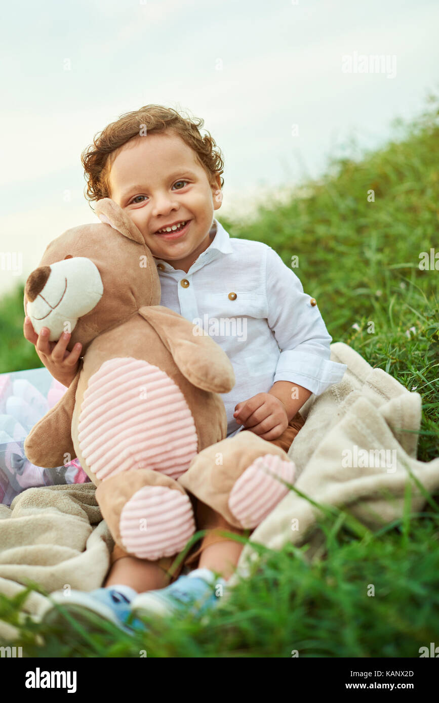 Ein junger spanischer Junge mit Teddybär sitzen auf Gras Stockfoto