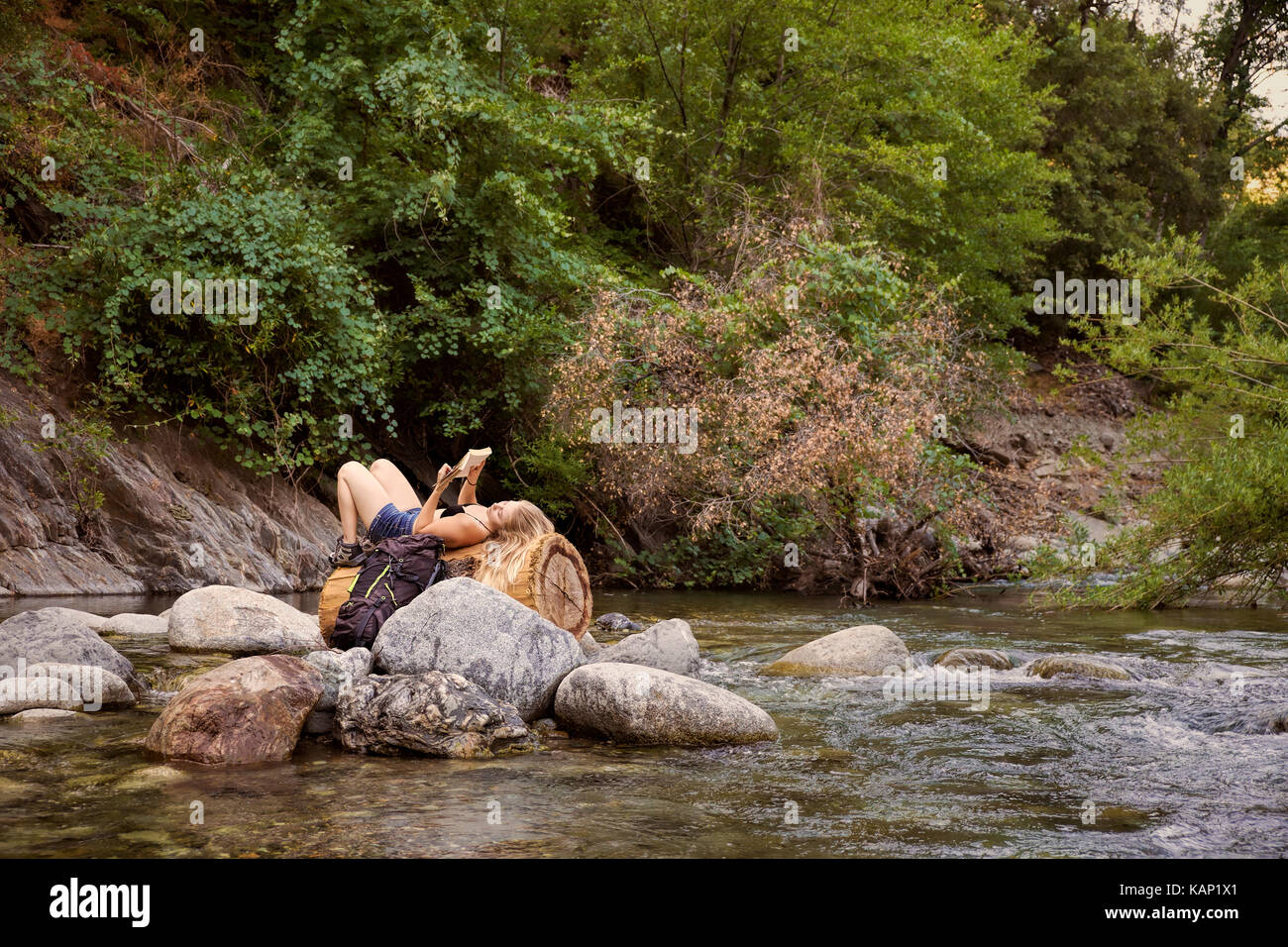 Eine weibliche Wanderer lesen und ruht auf einem toten Baum in der Mitte eines kleinen Mountain Creek in den Sierra Nevada Bergen in Nordkalifornien. Stockfoto