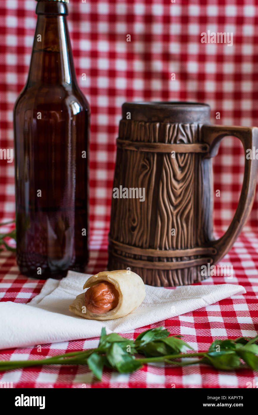 Hausgemachte Mini hot dog (Würstchen in Blätterteig) auf Serviette mit einer Flasche dunkles Bier und Steingut Tasse auf einem karierten Hintergrund Stockfoto