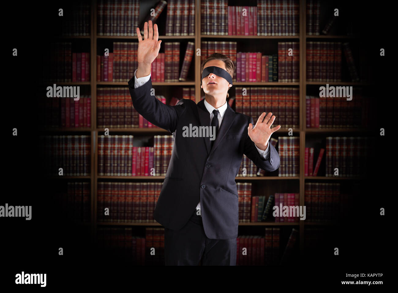 Mit verbundenen Augen junger Anwalt Gestik beim Stehen gegen Bücherregale im Büro Stockfoto