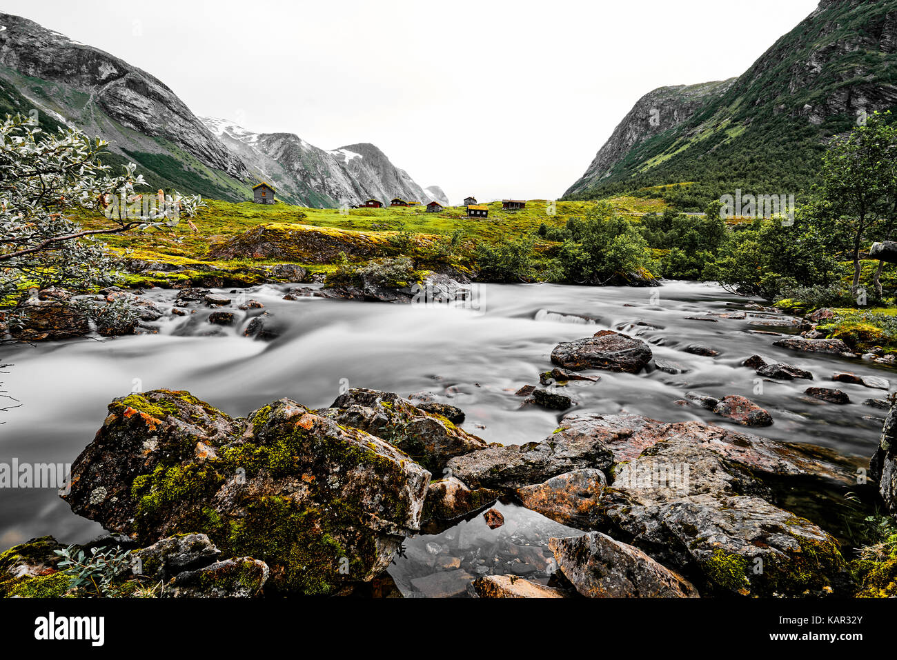 Lange Belichtung von gras dach Häuser in den Bergen von Norwegen mit grünen Wiesen und ein weißes Wasser Fluss im Vordergrund. Stockfoto