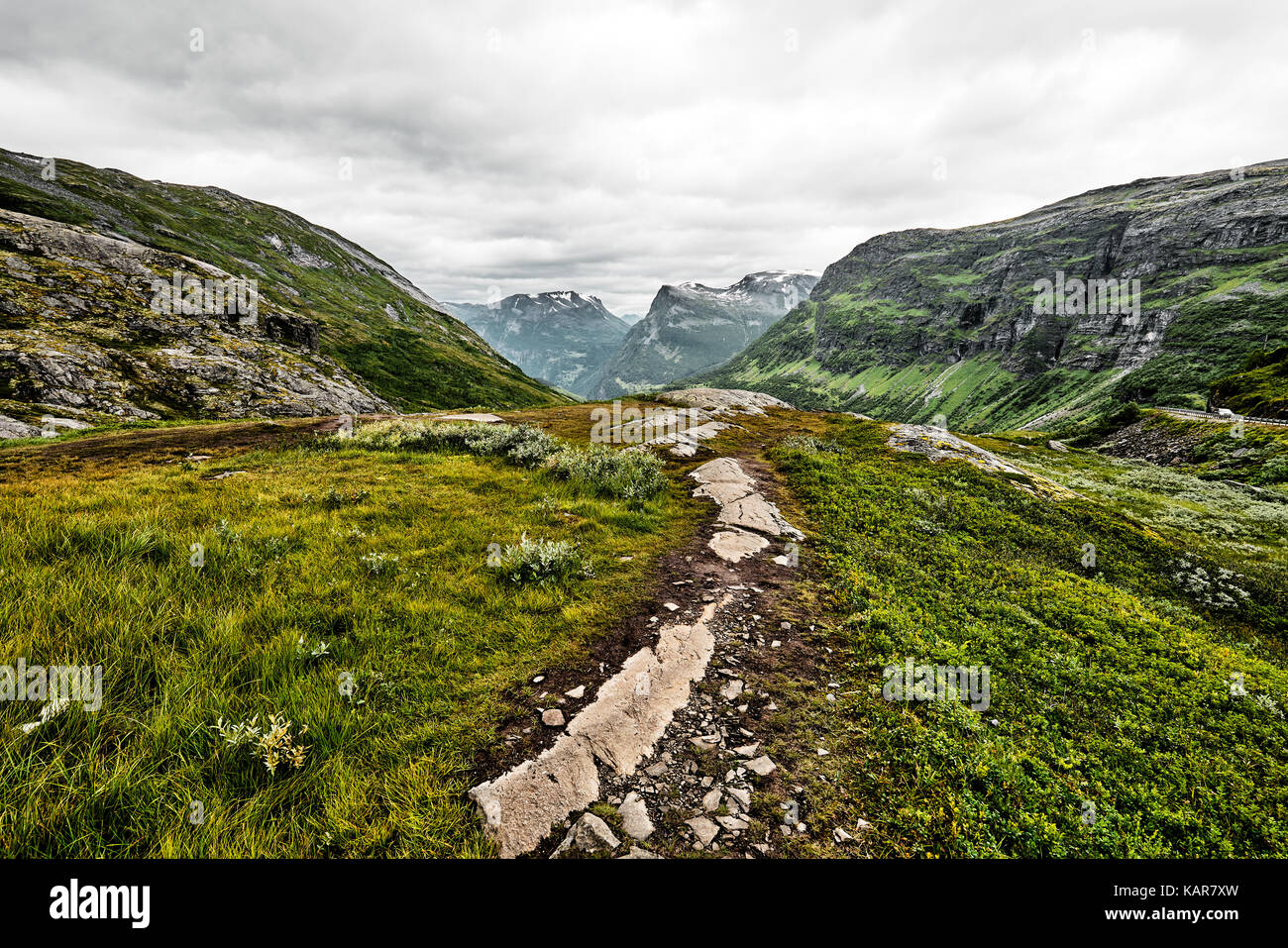 Über grüne Weide in den Bergen des westlichen Norwegen Pfad mit Schnee auf den Gipfeln und einem dunklen bewölkter Himmel Stockfoto