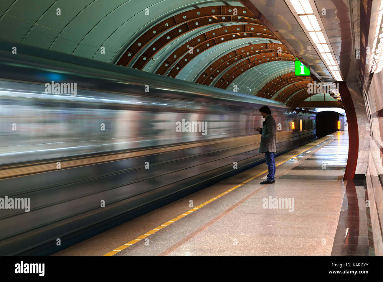 Einsamer junger Mann mit Smartphone Schuß von Profil bei der U-Bahn station mit verschwommenen fahrenden Zug im Hintergrund. Stockfoto