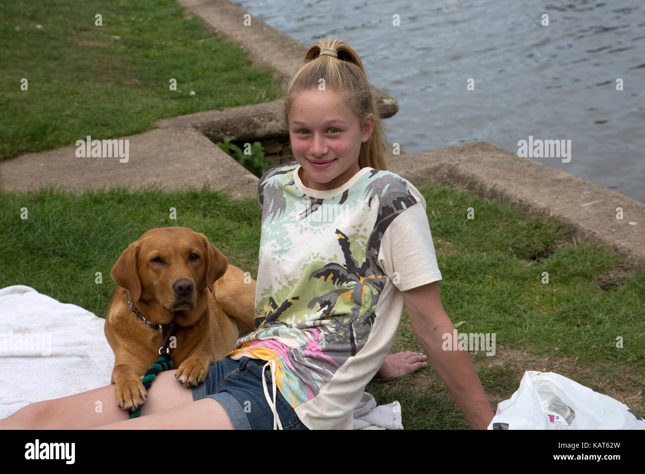 Lächelnde blonde Teenager sitzen mit Red fox Labrador Hund am Ufer Cotswolds uk Stockfoto