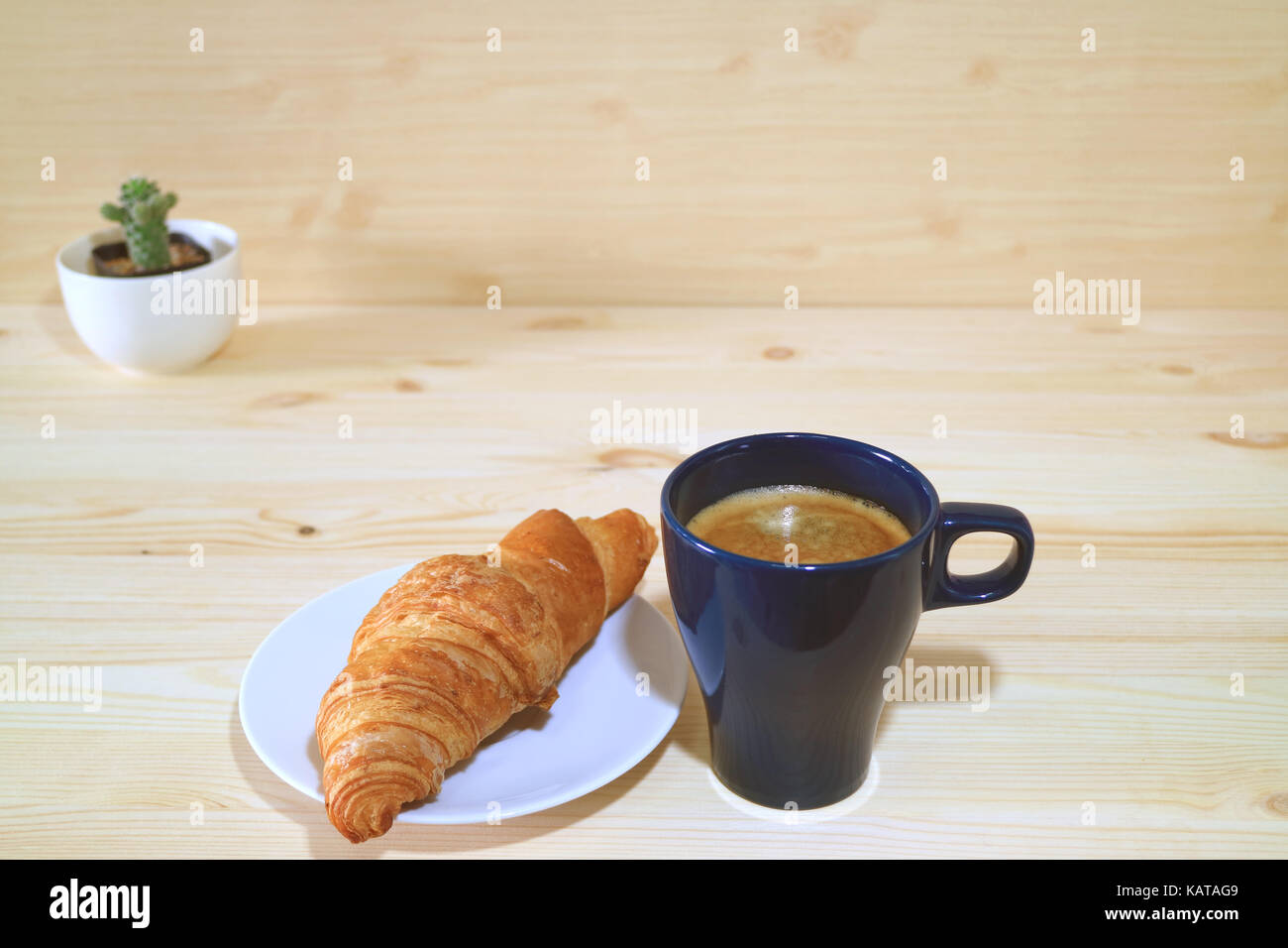 Eine Tasse Kaffee und einen Teller mit Butter Croissant serviert auf dem hölzernen Tisch mit einem niedlichen kleinen Kakteen Stockfoto