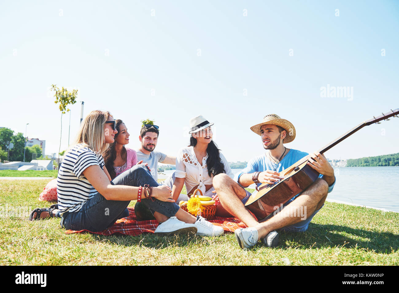 Glückliche junge Freunde mit Picknick im Park. Sie alle sind glücklich, Spaß, lächelnd und Gitarre spielen Stockfoto