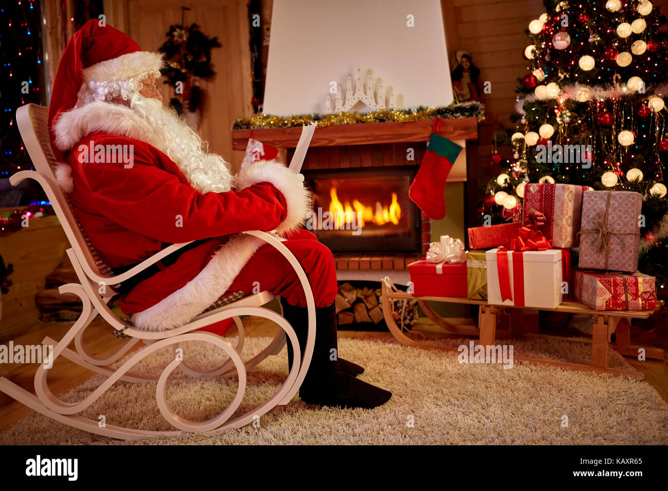 Real Santa Claus auf einem Schaukelstuhl in warmen Weihnachtsstimmung in liebevoll dekorierten Zimmer Stockfoto