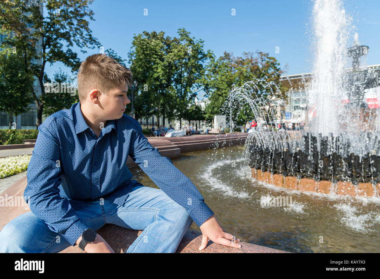 Teenager von 14 Jahren sitzt in der Nähe von Brunnen Stockfoto
