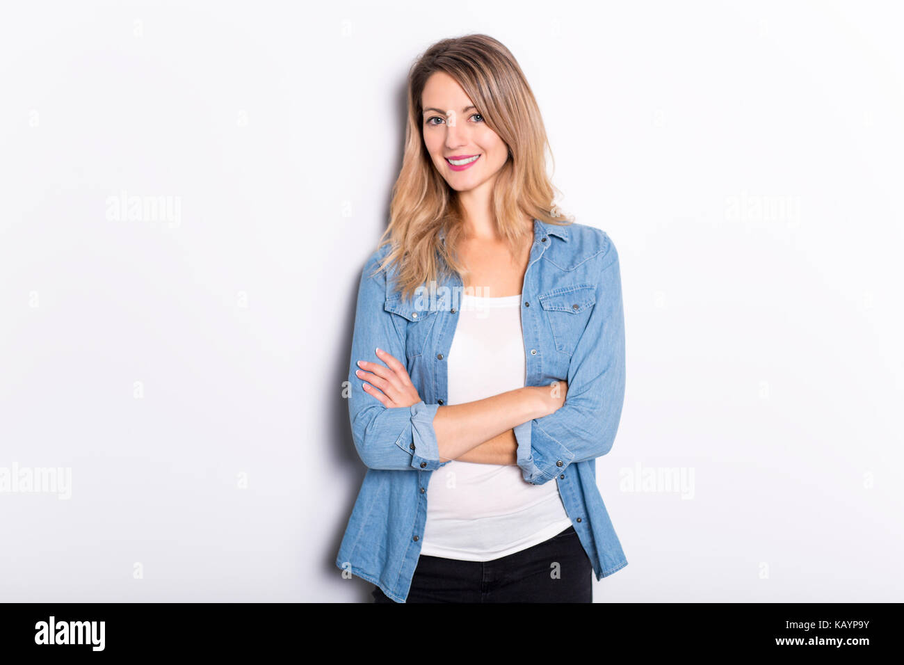 Junge Frau in Jeans Hemd und Jeans, lehnte sich gegen graue Wand Hintergrund Stockfoto