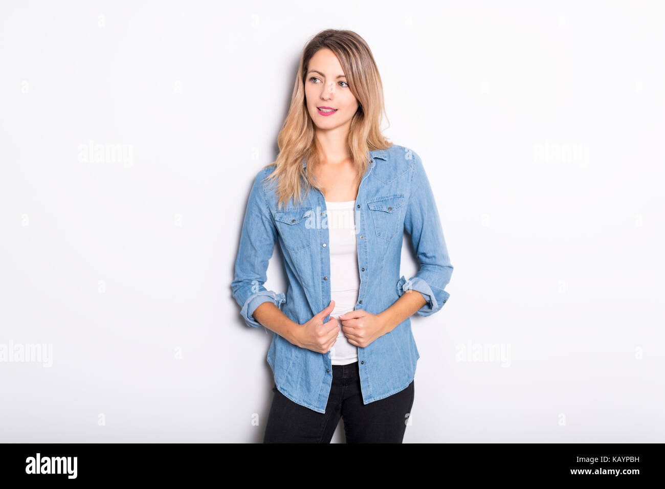 Junge Frau in Jeans Hemd und Jeans, lehnte sich gegen graue Wand Hintergrund Stockfoto
