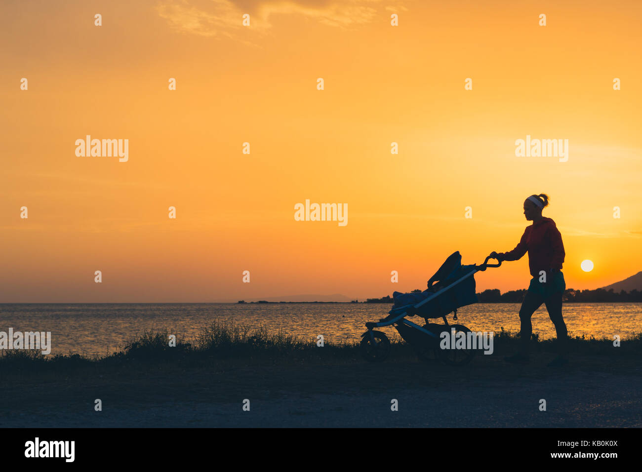 Mutter mit Kinderwagen zu Fuß am Strand genießen Mutterschaft bei Sonnenuntergang Landschaft. Joggen oder Walken Frau mit Kinderwagen. Schöne inspirierende Küste Stockfoto