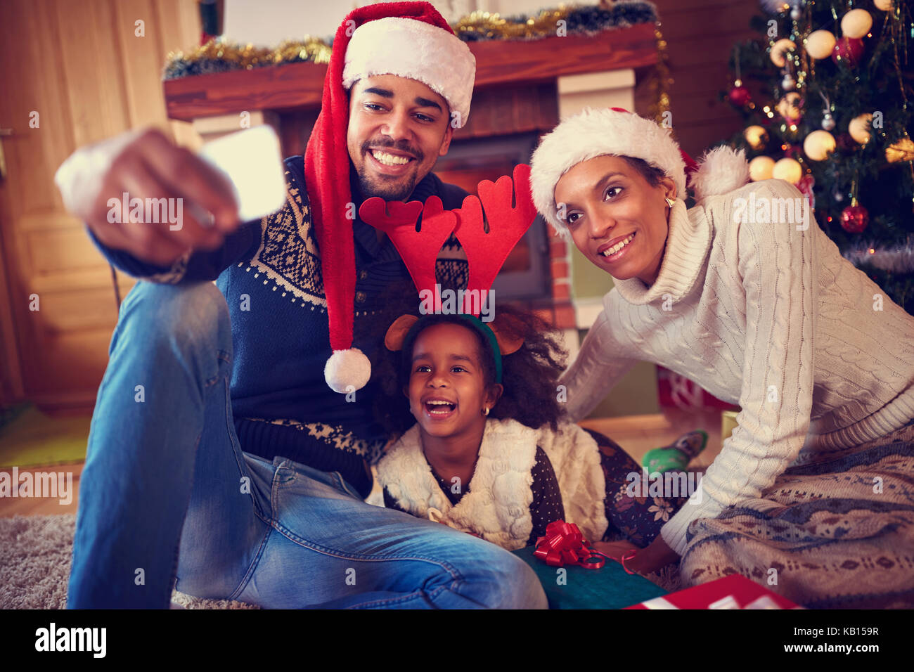 Lächelnde junge Familie in Weihnachtsstimmung, Foto mit Smartphone Stockfoto