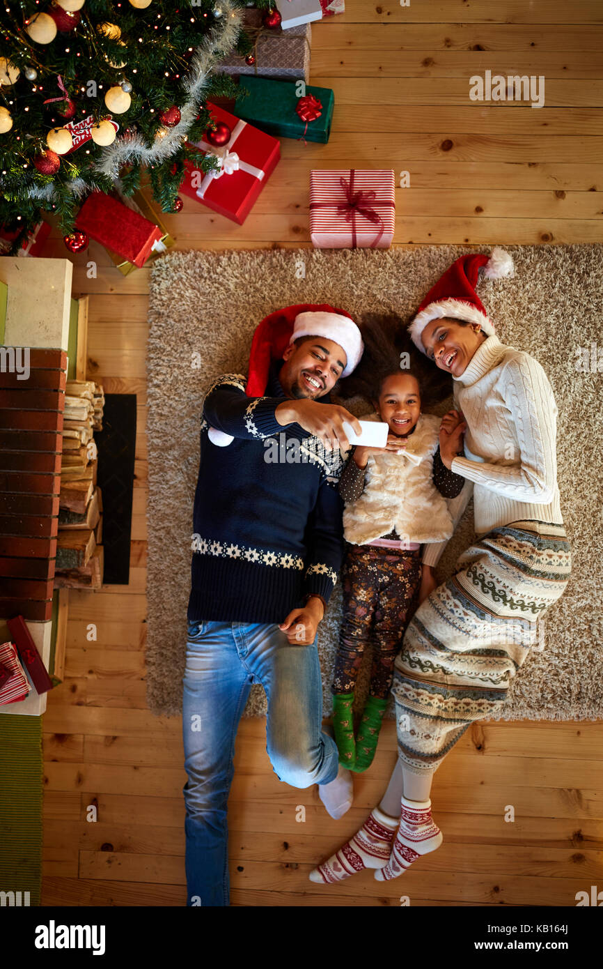 Weihnachtliche Atmosphäre, junge Familie liegen auf dem Boden, Ihre aus Holz und selfie Stockfoto