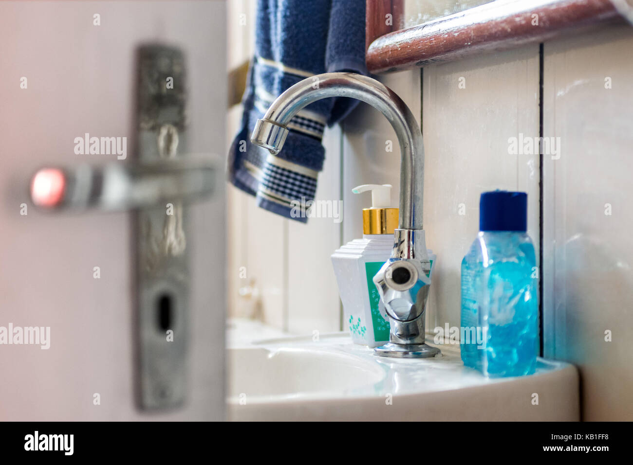 Innenraum eines Badezimmer, weiß gefliesten Wänden, Tür im Vordergrund, mit Verriegelung und Griff, ein weißes Waschbecken mit Wasserhahn, flüssige Seife, Spiegel Stockfoto