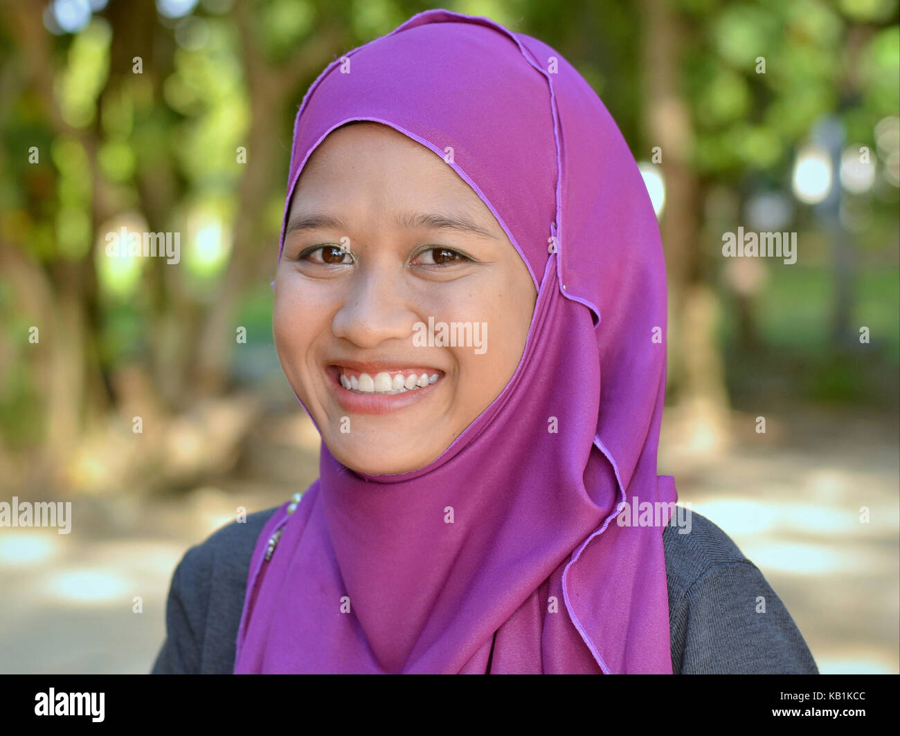 Schöne, junge muslimische Frau aus Malaysia, das Tragen eines stilvollen lila Hijab, wirft den berühmten MALAIISCHEN Lächeln Stockfoto