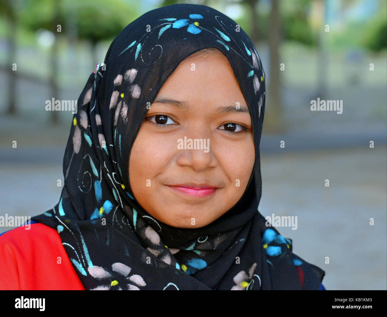 Muslimischen malaiischen Mädchen (Teenager) mit lächelnden Augen, trägt einen eleganten schwarzen Kopftuch mit modernen Floral Design Stockfoto