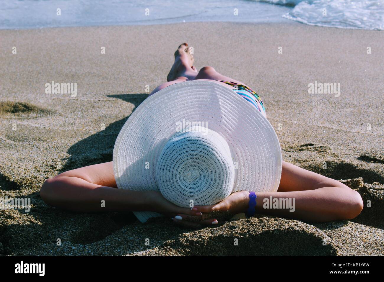 Die Frau liegt auf dem Sand vor dem Hintergrund des Meeres Brandung in einem weißen Hut mit breiter Krempe. Stockfoto