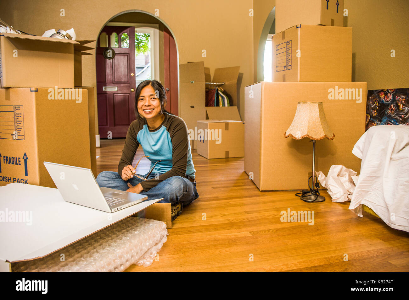 Das Porträt einer jungen asiatischen Frau sitzt auf dem Boden vor einem Laptop von Kisten, als ob Sie in oder out ist, umgeben. Stockfoto