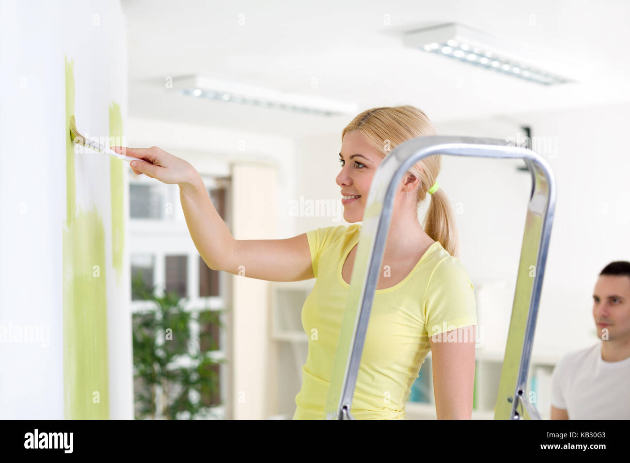 Lächelnde Frau Malerei Wand und stehen auf einer Leiter Stockfoto