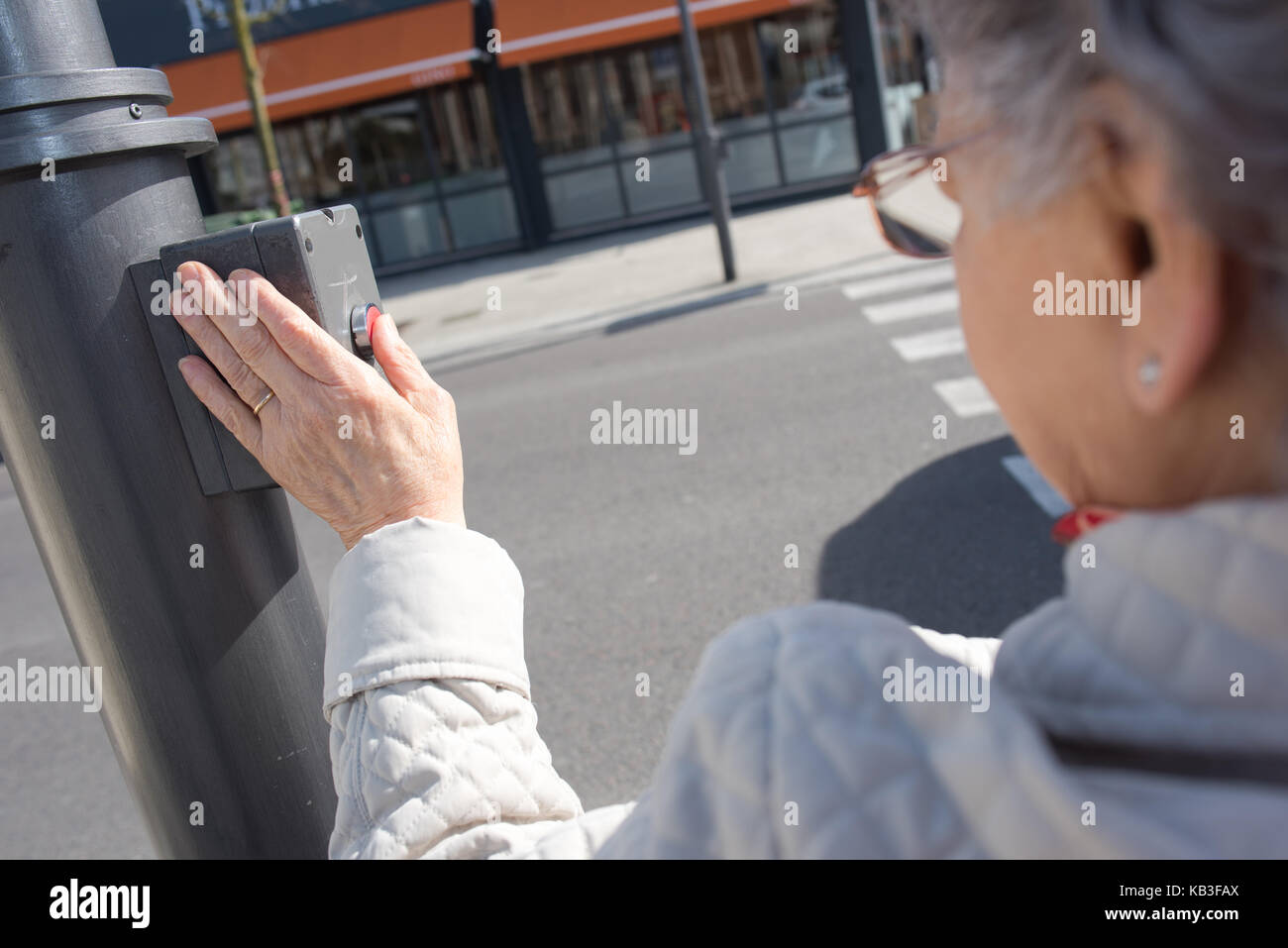 Alte Dame durch Drücken der Taste an der Ampel am Zebrastreifen Stockfoto