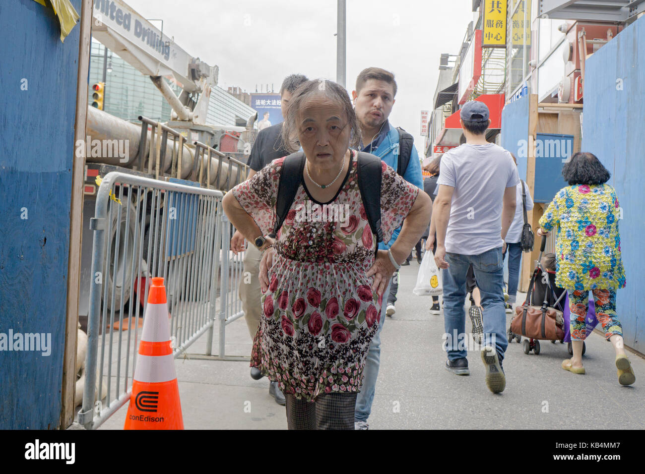 Eine ältere chinesische Frau hinunter Hauptstraße mit einem ernsten Ausdruck in Chinatown, Flushing, Queens, New York City. Stockfoto