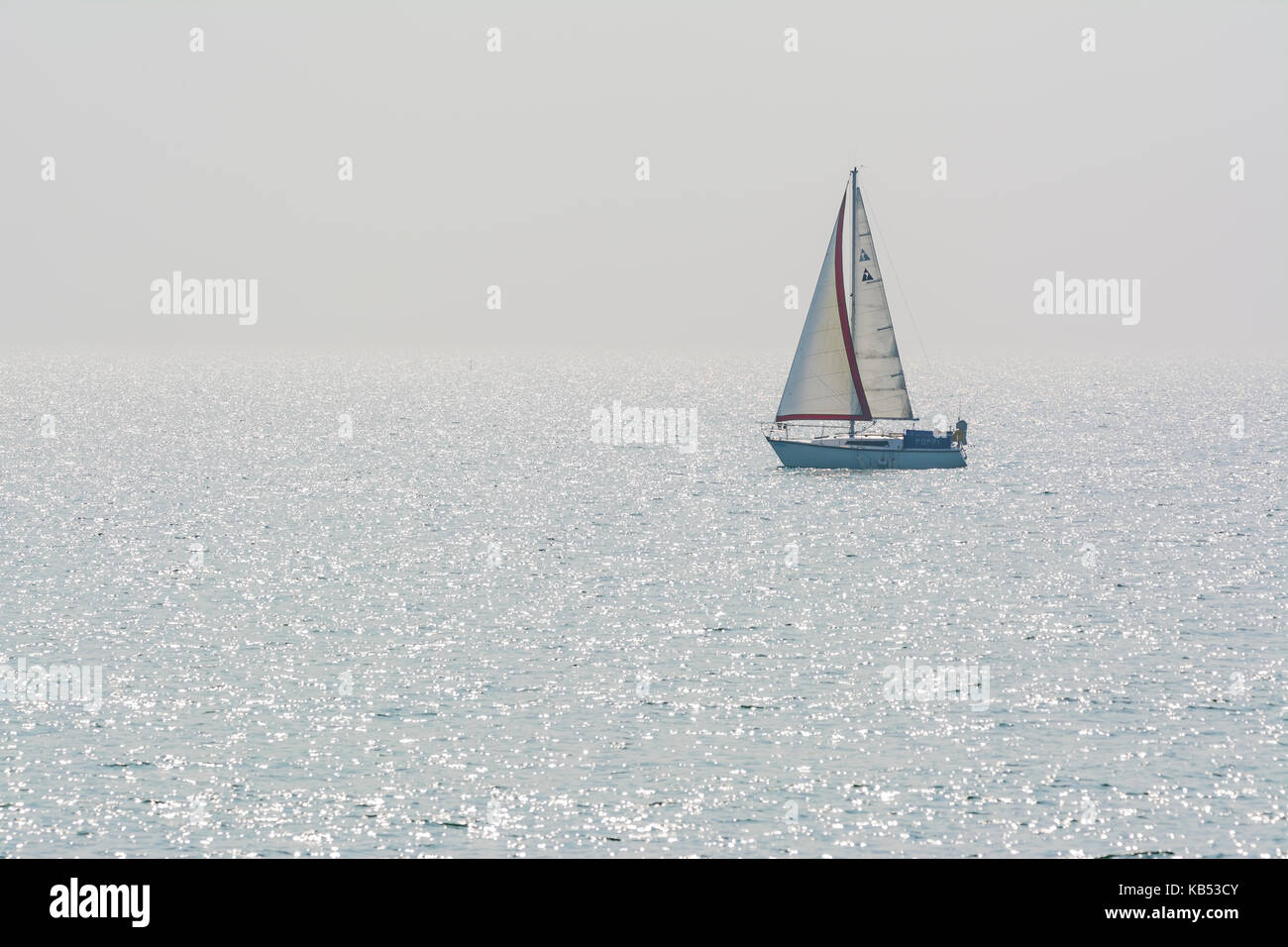 Kleine Yacht auf dem Meer mit Sonne funkelnde im Wasser. Kleines Segelboot auf dem Ozean mit reflektierenden Sonne funkelt. Stockfoto