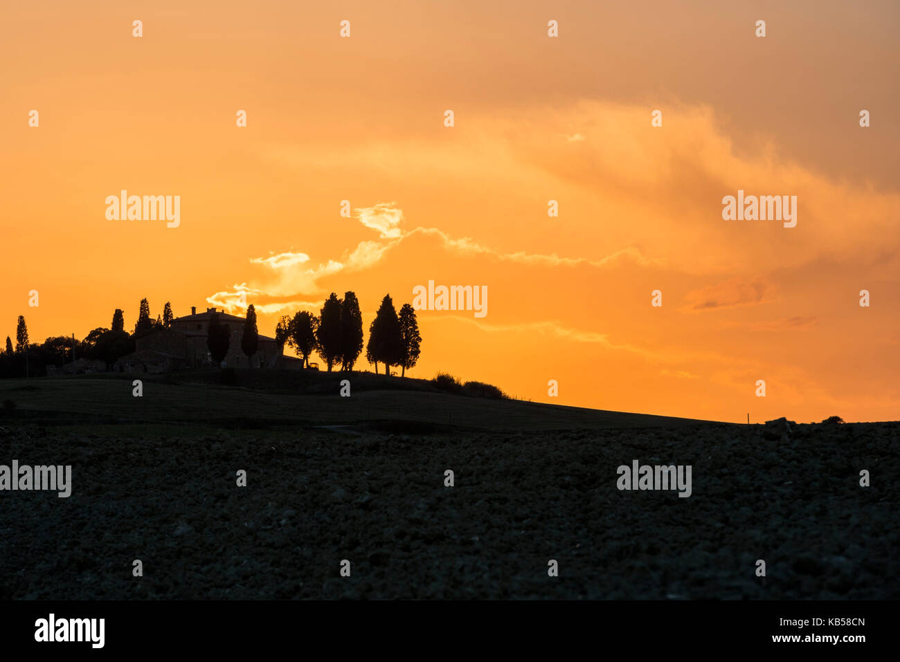 Ein kontrast Silhouette einer Villa, die von Zypressen umgeben, auf der flammend roten Abend Himmel mit Wolken Stockfoto
