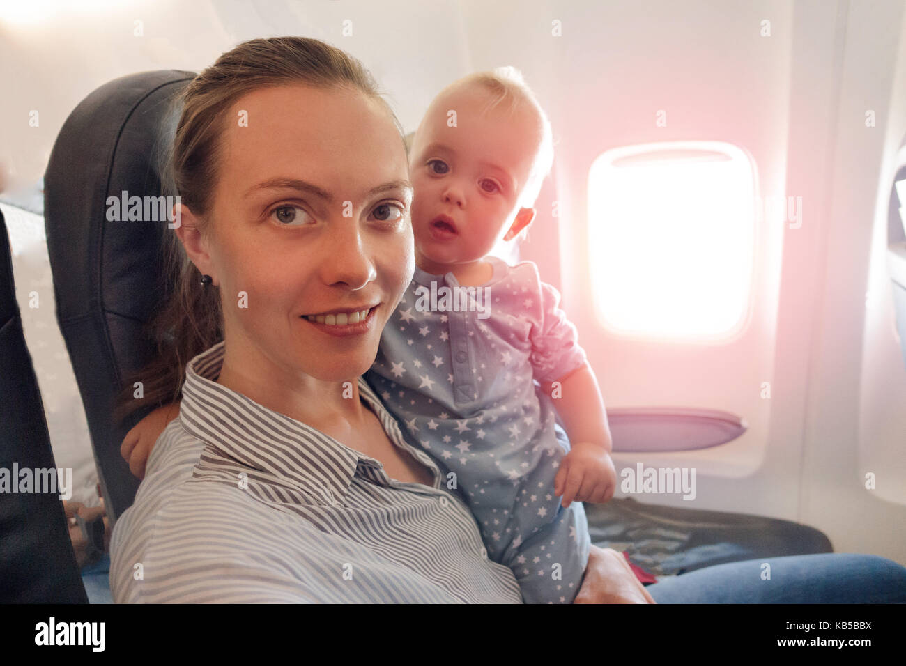 Mutter und Baby Reisen im Flugzeug Blick an Kamera Stockfoto