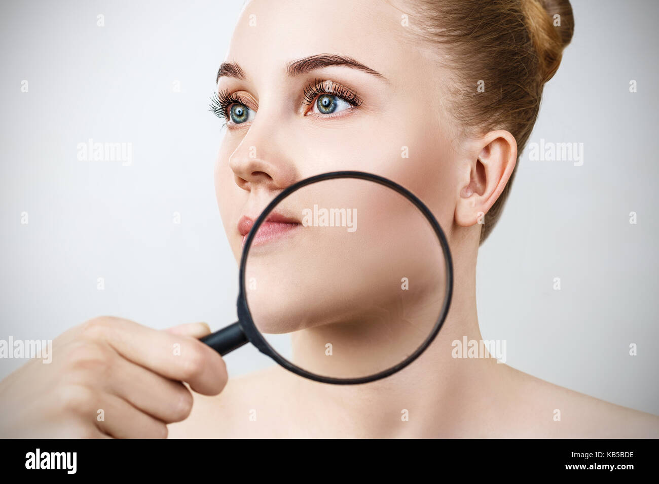 Junge Frau mit Lupe prüfen Haut Stockfoto