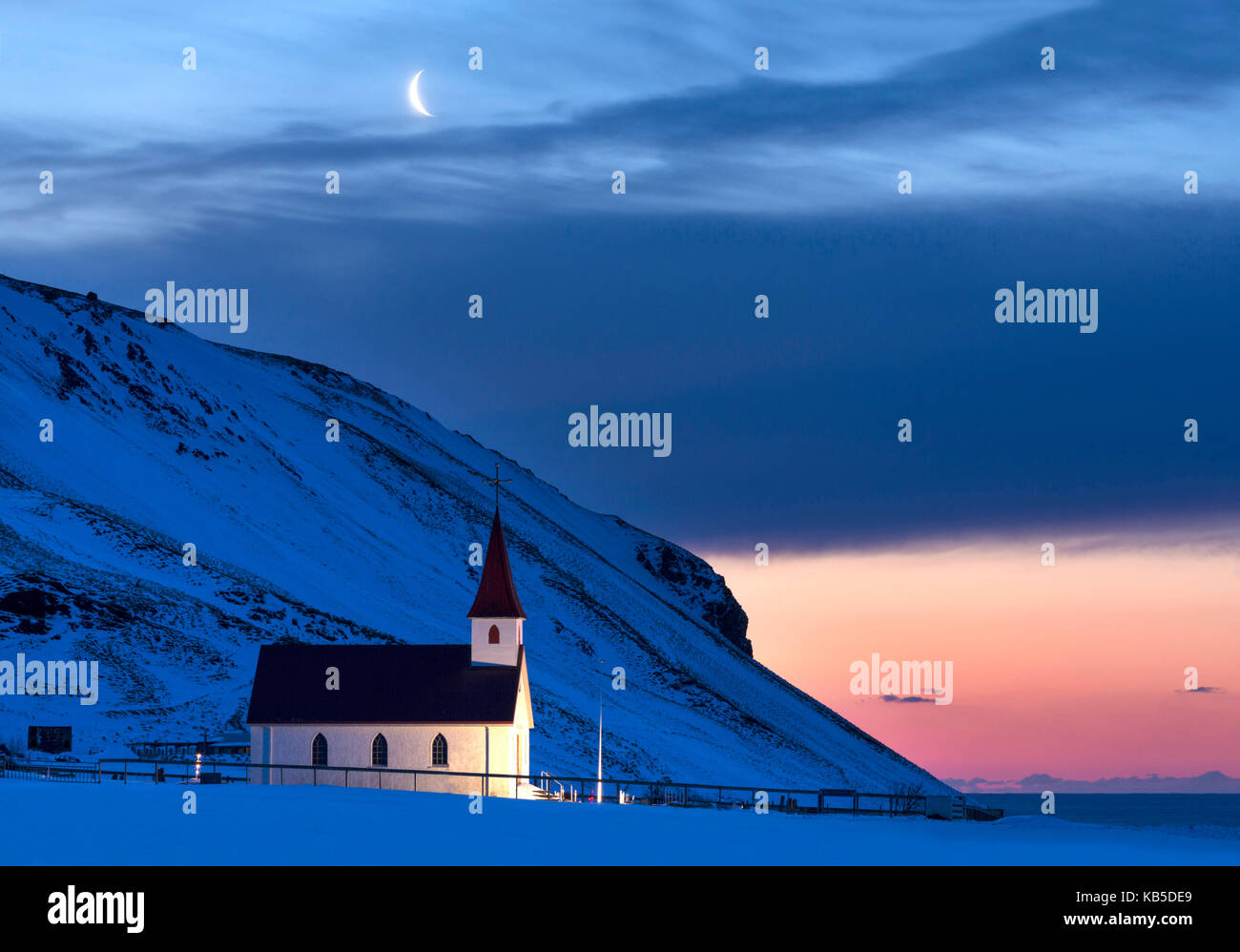 Beleuchtete Kirche in der Dämmerung gegen Schnee bedeckte Berge, Winter, in der Nähe von Vik, South Island, Polargebiete Stockfoto