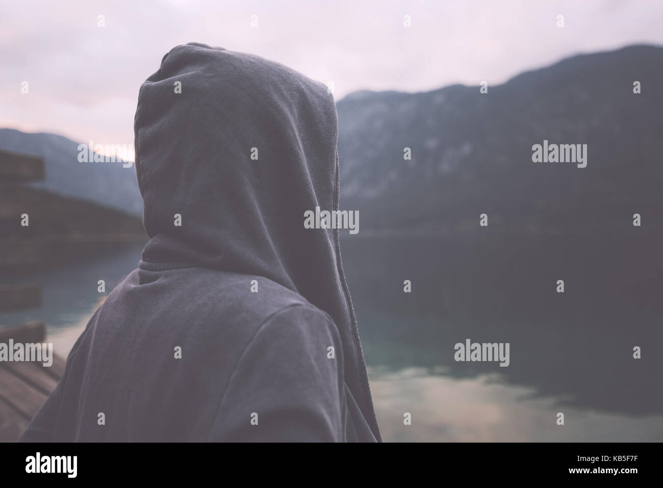 Düstere nostalgische Portrait von traurig einsam melancholisch erwachsene Frau mit Kapuzenjacke stehend am Ufer des Sees in Misty bewölkten Morgen und Denken Stockfoto