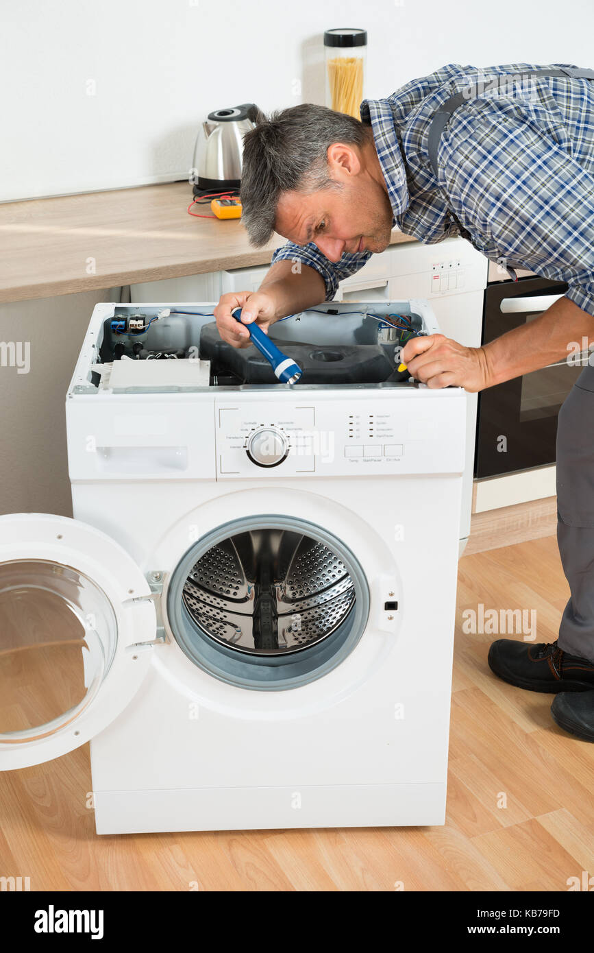 Die ganze Länge der Heimwerker Kontrolle Waschmaschine mit Taschenlampe in der Küche Stockfoto