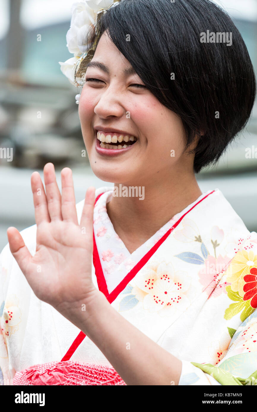 Japan. Kopf und Schultern geschossen von Jungen lachen japanischen Frau in cremefarbenen Kimono. Weiße Blumen im Haar. Hand gehalten, um im 'nein, stopp' Geste. Stockfoto