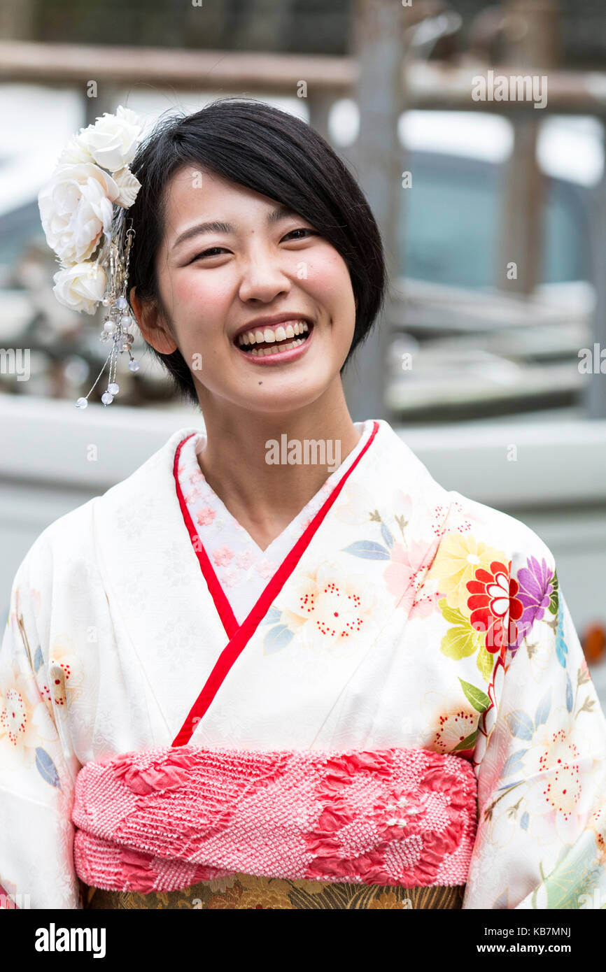 Japan. Kopf und Schultern geschossen von Jungen lachen japanischen Frau in cremefarbenen Kimono. Weiße Blumen im Haar. Mit Blick auf Stockfoto