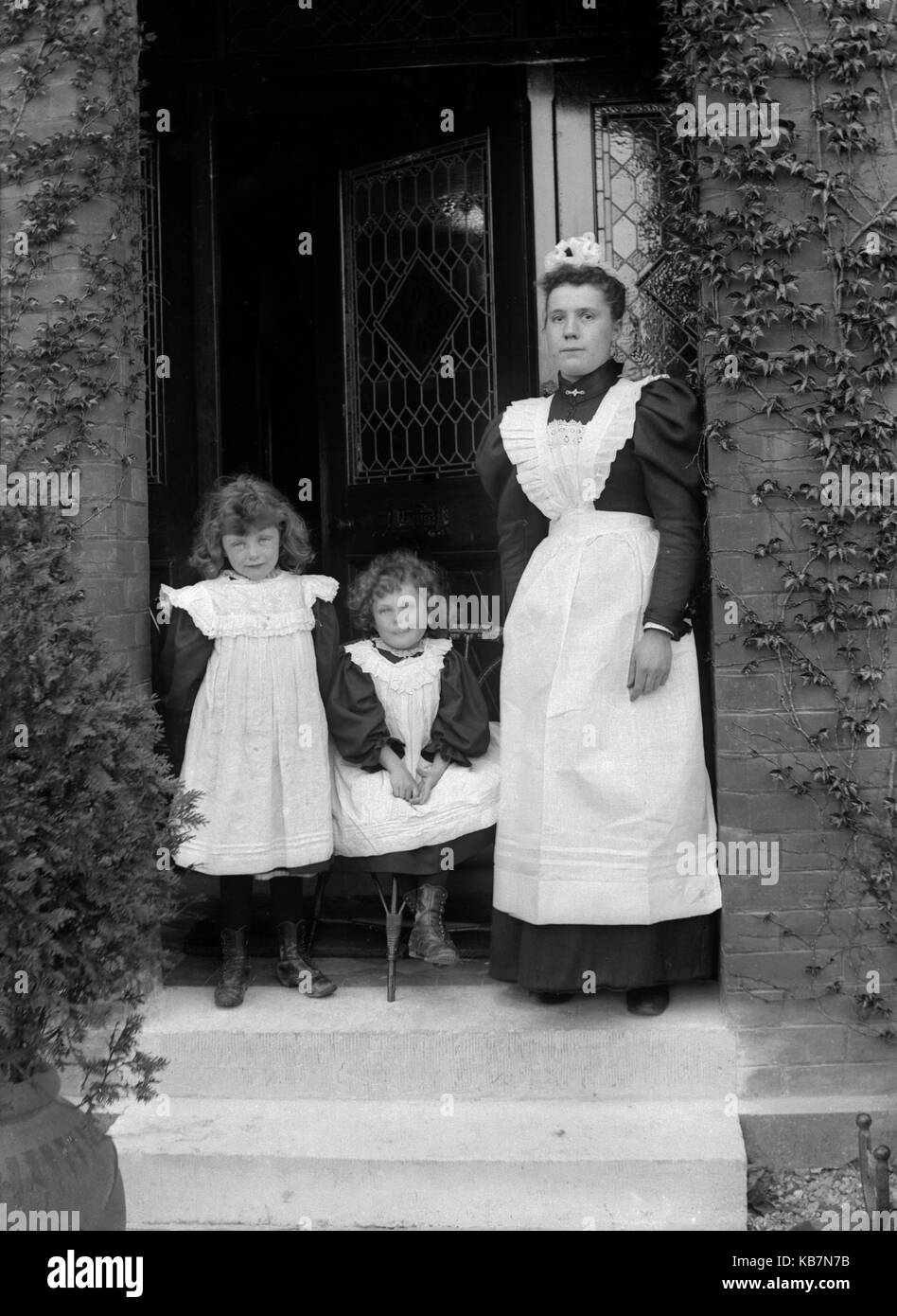 AJAXNETPHOTO. 1890 - 1914 (ca.). Ort unbekannt. - Hausmädchen UND ZWEI KINDER für die Kamera posiert vor der Tür eines Hauses, EIN KIND SITZT. Fotograf: unbekannt © DIGITAL IMAGE COPYRIGHT AJAX VINTAGE BILDARCHIV QUELLE: AJAX VINTAGE BILDARCHIV SAMMLUNG REF: AVL 172109 6 Stockfoto