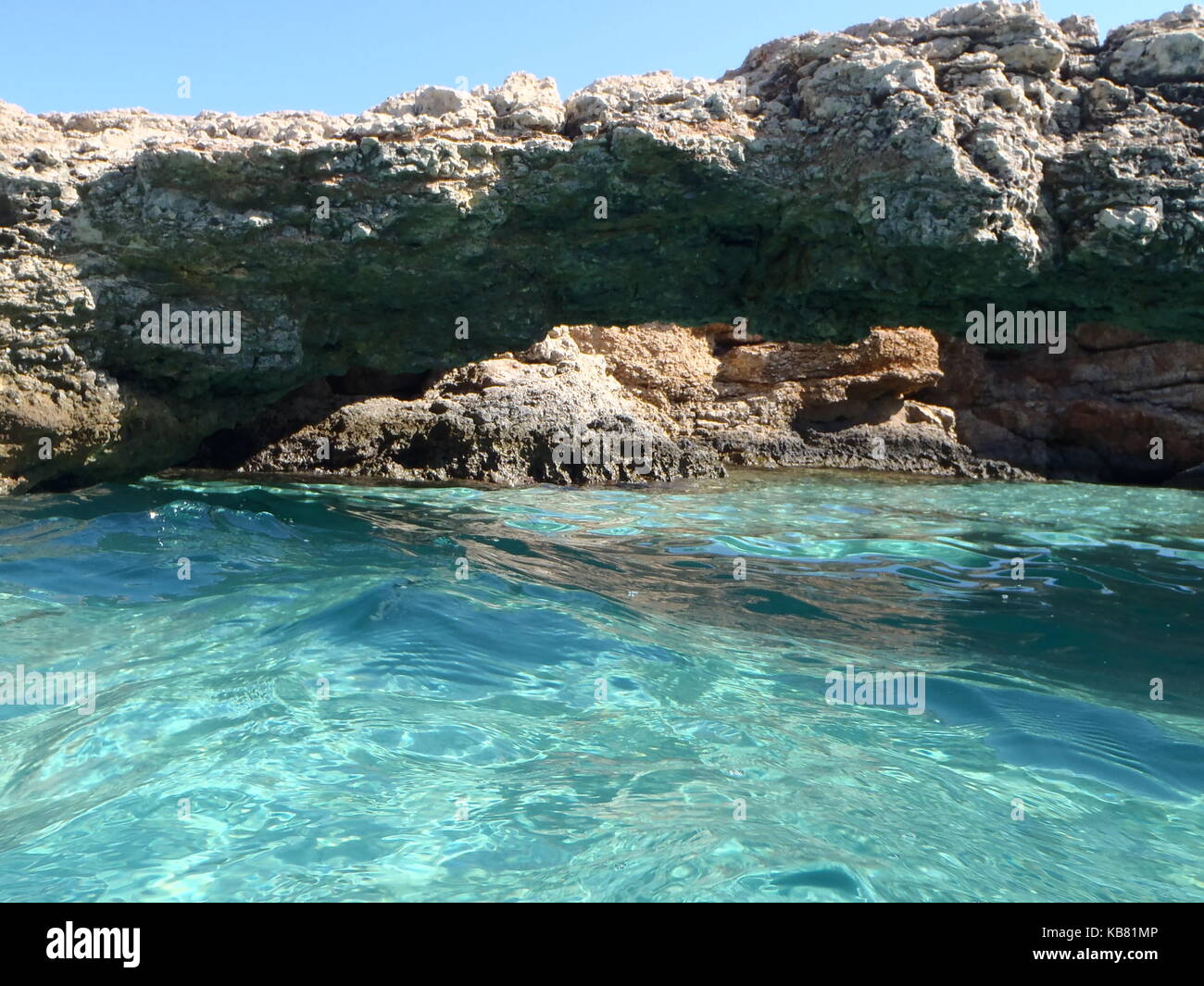 Ein Foto von dem türkisfarbenen kristallklaren Wasser der Blue Lagoon, Malta, mit weißem Sand und einem Felsvorsprung Bogen über das Wasser und blauem Himmel Stockfoto