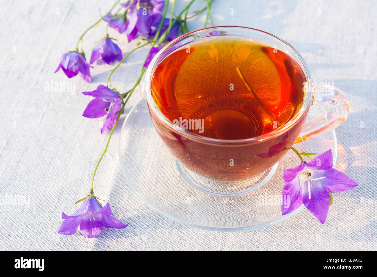 Glas Tee Tasse und Blue Bell Blumen auf dem Leinen Servietten Stockfoto