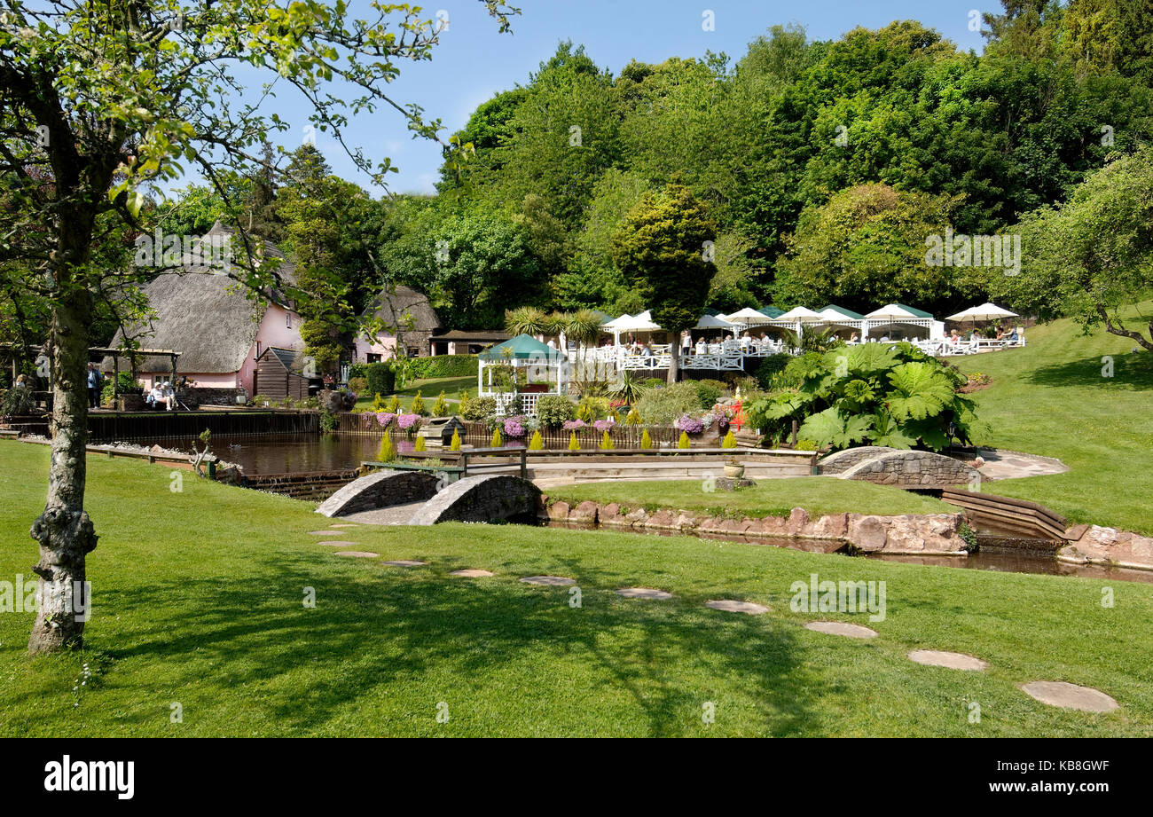 Rose Cottage Tea Gardens, cockington, Torquay Devon, Großbritannien - Blick über den Rasen und Stream mit, Kaffee Terrassen, strohgedeckten Kinderbett und Musikpavillon im Hintergrund Stockfoto